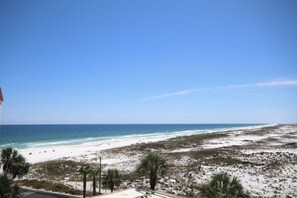 A beach view with a clear sky, sandy beach, and sparse vegetation.