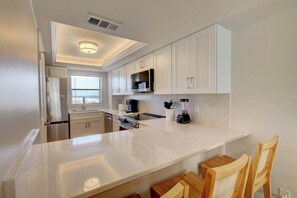Une cuisine moderne avec des meubles blancs, un îlot central et un four à micro-ondes encastré.