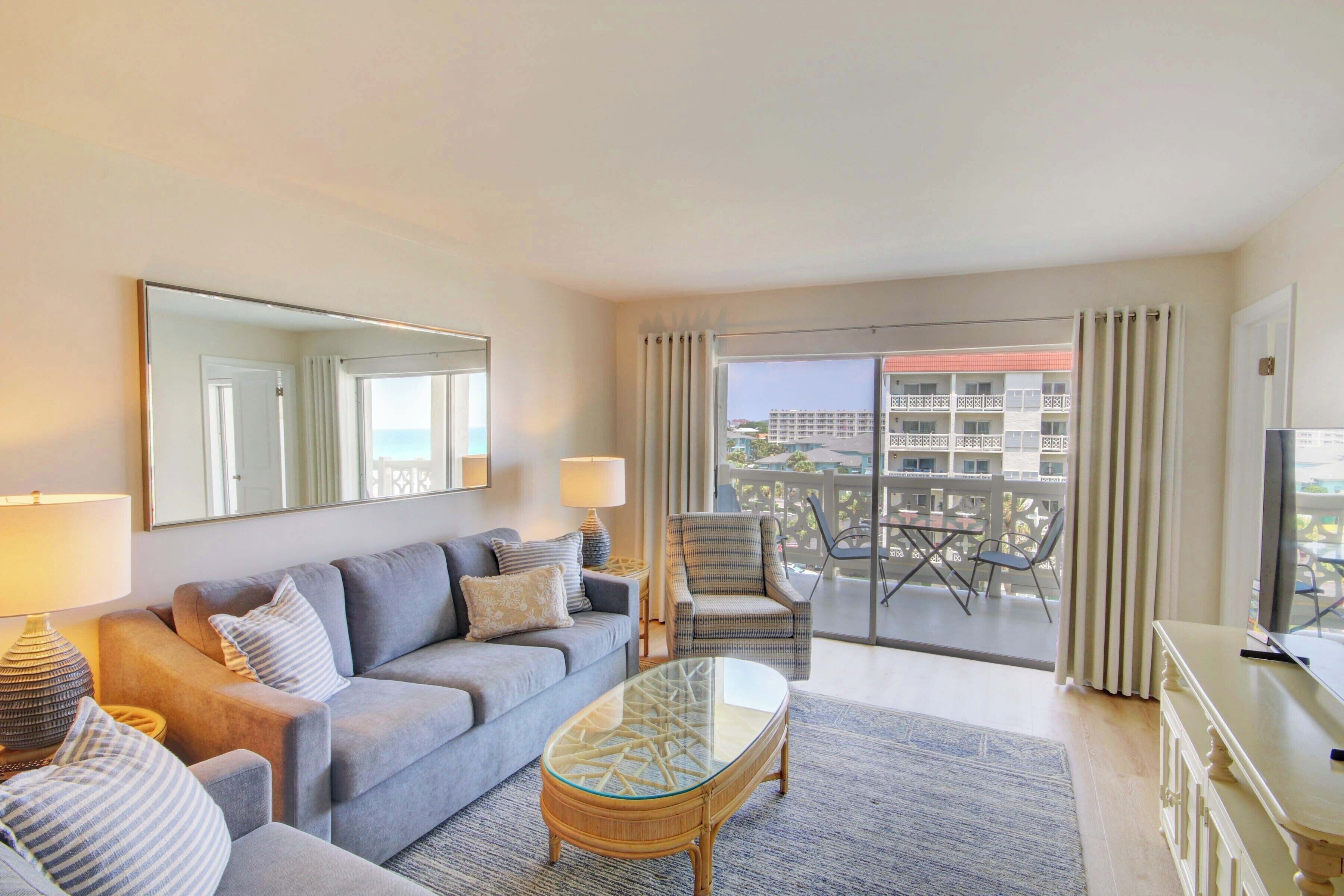 Ein modernes Wohnzimmer mit Sofa, Sessel, Glastisch und einem Balkon mit Blick auf Gebäude.