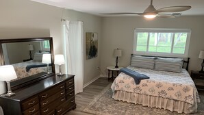 A bedroom with a large bed, a dresser, a chair, a ceiling fan, and a window with a view of greenery. - Upgraded and updated Villa in Tranquil Neighborhood (Rotonda West)