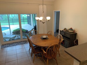 A dining area with a wooden table and chairs, a chandelier, and a view of a swimming pool through large glass doors.