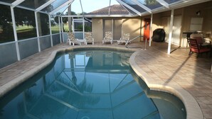 A swimming pool with a glass enclosure, surrounded by chairs and a covered patio area. - Upgraded and updated Villa in Tranquil Neighborhood (Rotonda West)