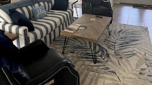 A spacious living room with a striped sofa, a black armchair, and a coffee table. There is a kitchen area with cabinets and a dining table in the background. - Upgraded and updated Villa in Tranquil Neighborhood (Rotonda West)