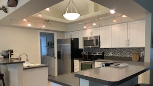 A modern kitchen with white cabinets, a central island, stainless steel appliances, and pendant lighting. - Upgraded and updated Villa in Tranquil Neighborhood (Rotonda West)
