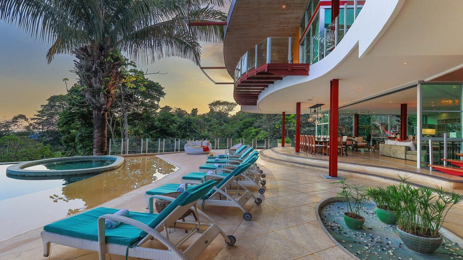 A modern hotel with a pool area, lounge chairs, and a dining area with red pillars.