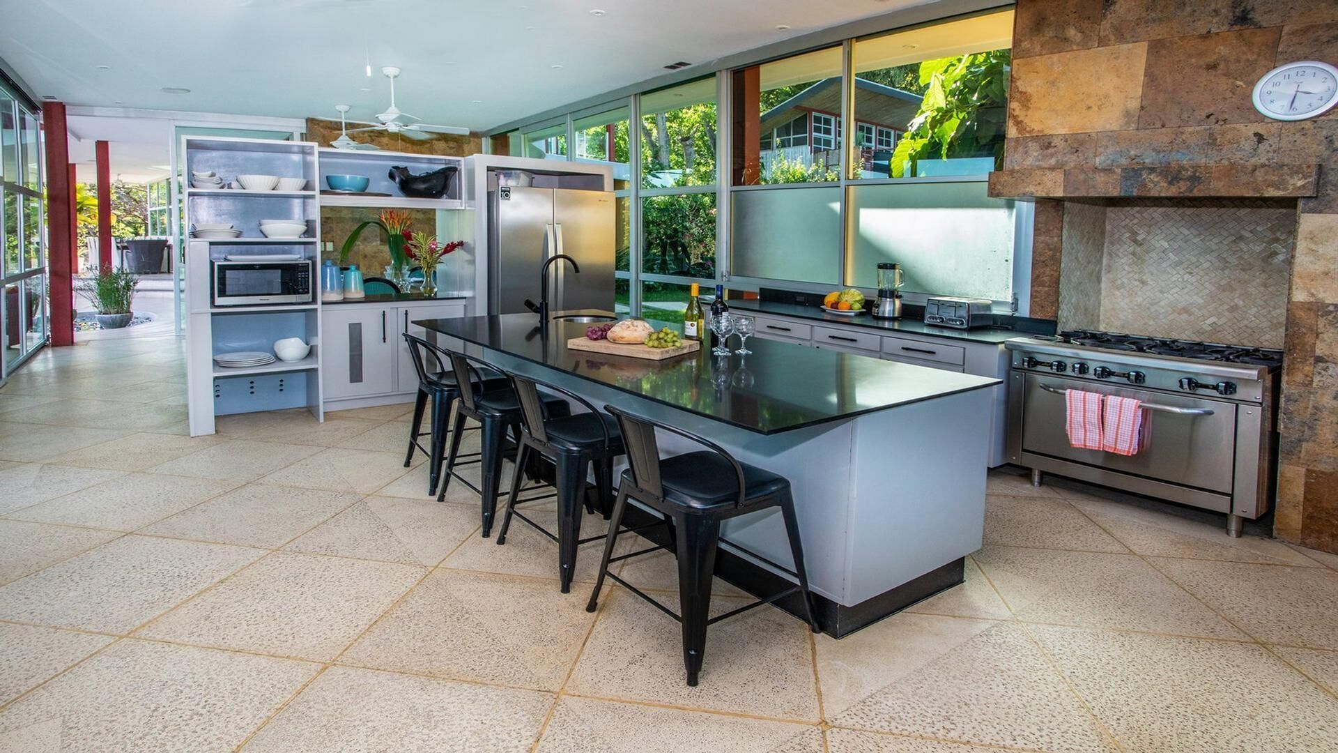 A modern kitchen with a central island, bar stools, a built-in oven, and a stone fireplace.