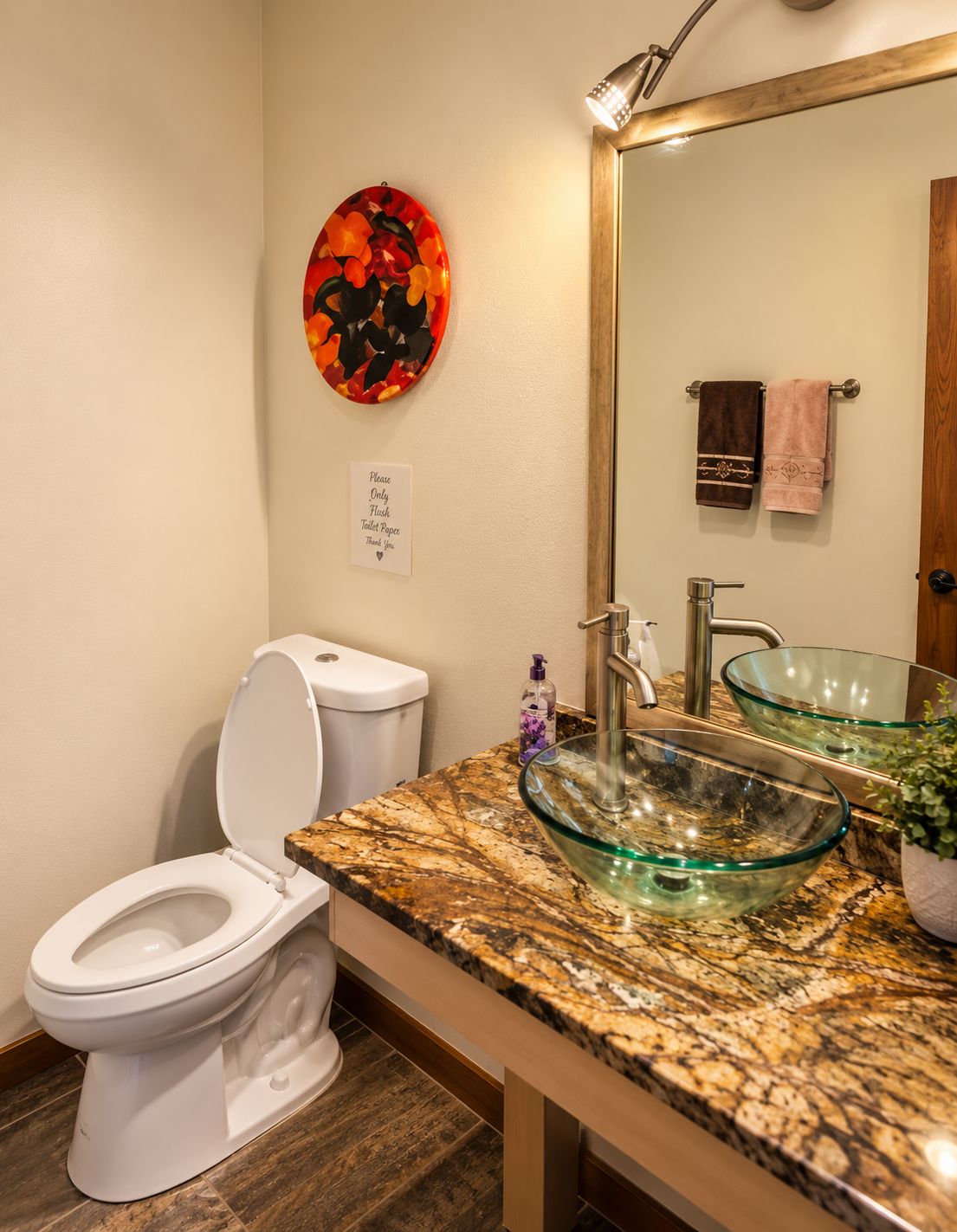 Un baño con inodoro, lavamanos tipo cuenco de vidrio, encimera de mármol, espejo montado en la pared y un plato decorativo.