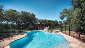 Una piscina con solárium de piedra, rodeada por una valla y árboles.