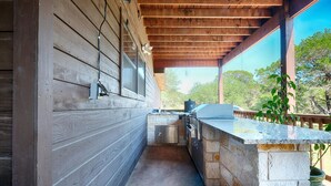 Una cocina exterior con encimera de piedra, una parrilla y un fregadero.