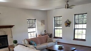 Amplia sala de estar con chimenea, un sofá grande, una mesa de centro y dos ventanas con persianas.