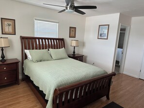A bedroom with a wooden bed, two bedside tables with lamps, a ceiling fan, and framed pictures on the walls. - Closest home on water to Beach Access! 5 min walk. Private heated Pool. Dock (Marco Island)