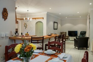 Ein Essbereich mit einem Tisch für vier Personen, einer Chandelüster und einem Fernseher im Hintergrund.