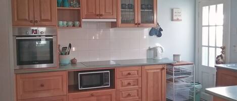 A kitchen with wooden cabinets, a stainless steel oven, a microwave, and a kettle on the countertop.
