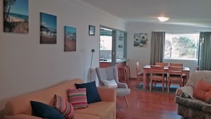 Una sala de estar con un sofá, sillones, una mesa de comedor con sillas y obras de arte en las paredes.