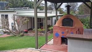 Un patio trasero con una zona de barbacoa de ladrillo, un porche cubierto y una casa con panel solar.