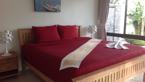 Ein Schlafzimmer mit einem hölzernen Bett, roter Bettwäsche, einem Bild an der Wand und einem Fenster mit Vorhängen.