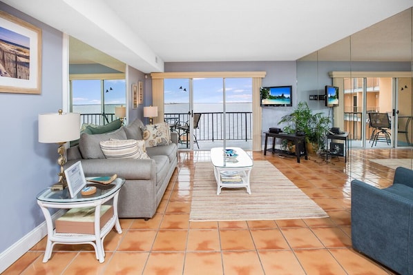 Una sala de estar con sofá, una mesa de centro y televisión. Hay un balcón con vista al mar.