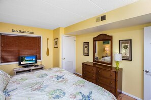 A bedroom with a bed, a television on a stand, a dresser, and a mirror.