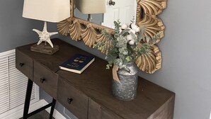 A wooden console table with a mirror, a starfish, a book, and a vase with flowers.