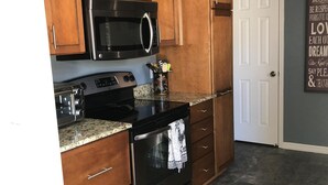 A kitchen with wooden cabinets, a black microwave, a stove, and a granite countertop.
