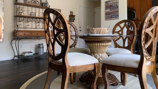 A dining area with wooden chairs and a central table, surrounded by a kitchen area with wooden cabinets and a chandelier.