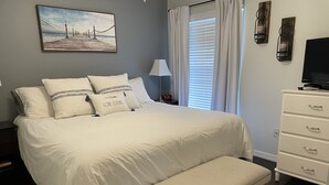 A neatly arranged bedroom with a large bed, a bedside table, a lamp, a bench, and a TV.