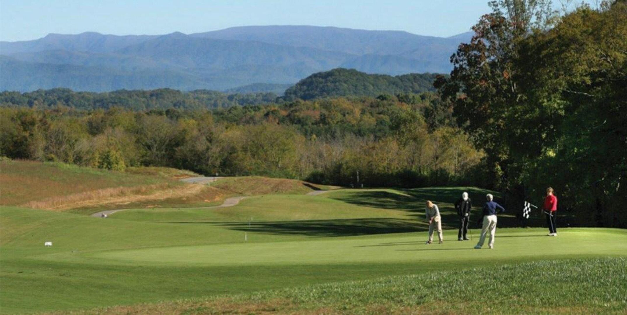 Un campo de golf con una vista despejada del paisaje circundante, incluyendo montañas y árboles a lo lejos.