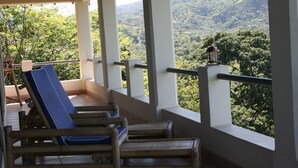Een balkon met rieten meubilair en uitzicht op een beboste helling.