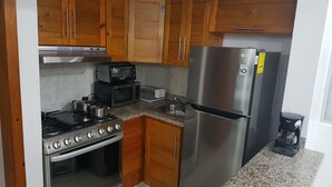 Cocina compacta con gabinetes de madera, refrigerador de acero inoxidable, horno empotrado, microondas y estufa a gas.