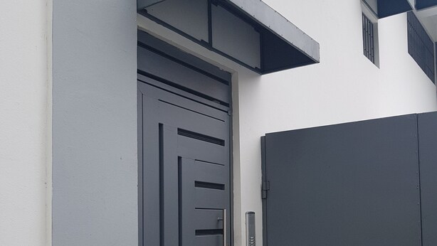 Una entrada moderna a un edificio con una puerta gris y un escalón pequeño que lleva a un felpudo.