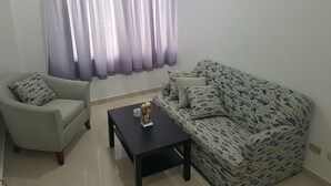 Una sala de estar con un sofá, dos sillones, una mesa de centro y un ventanal con cortinas.