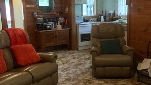 A cozy living room with a fireplace, a wooden cabinet with various items, and a kitchen area in the background.