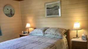A neatly made bed with a patterned quilt, two bedside lamps, a framed picture on the wall, and a small wooden cabinet with a tissue box on the nightstand.