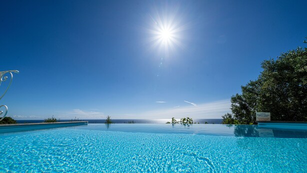Klar blå himmel, strålende sol og en swimmingpool med havudsigt.
