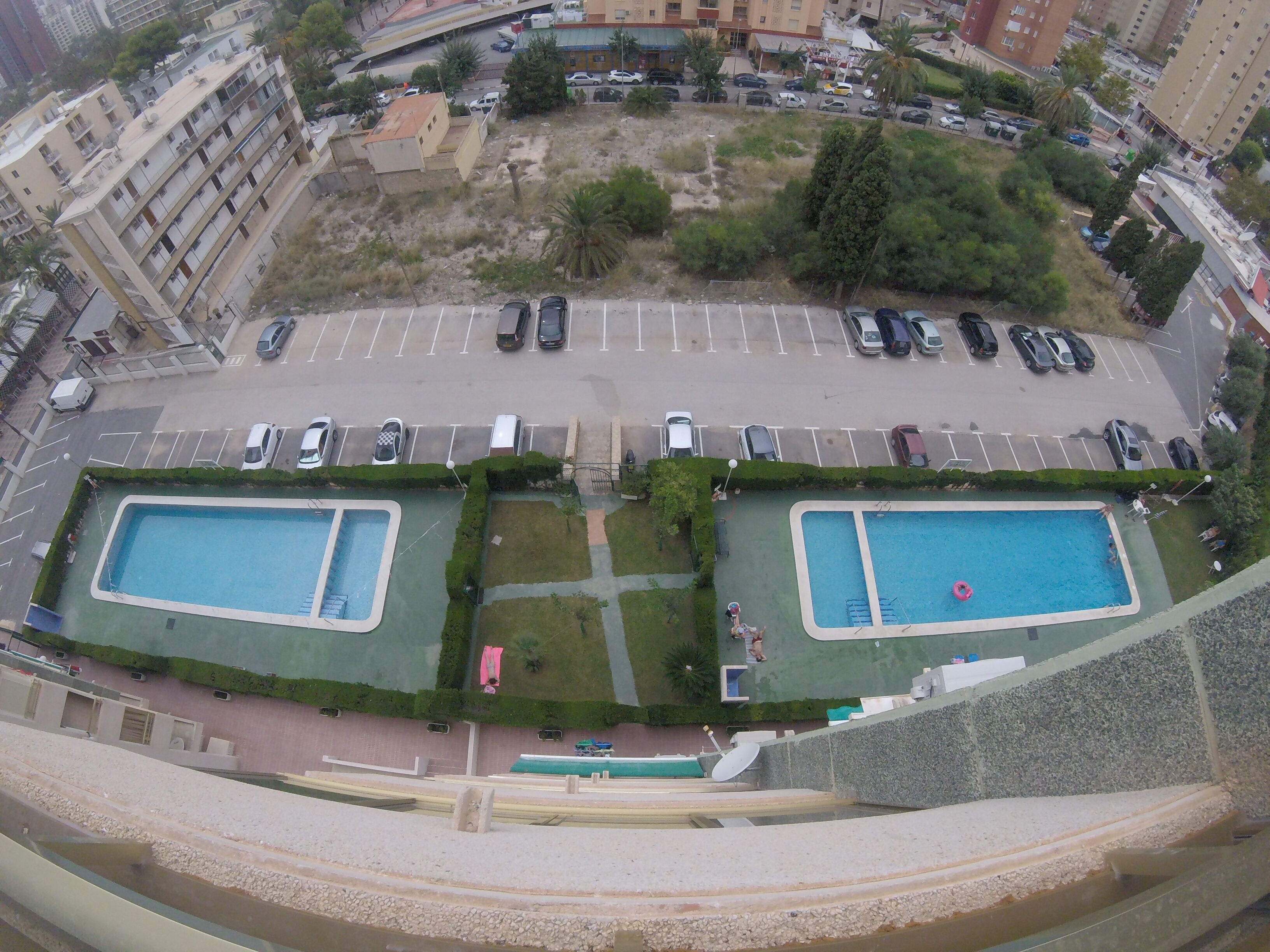 Un edificio de gran altura con dos piscinas, estacionamiento y áreas verdes circundantes.