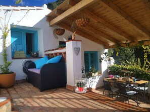 Ein gemütlicher Patio-Bereich mit einem Rattan-Sofa, einem Holztisch und Topfpflanzen.