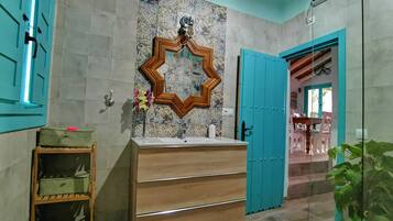 Een badkamer met een houten wastafelmeubel, een spiegel met een geometrisch lijstwerk, en een blauwe deur.