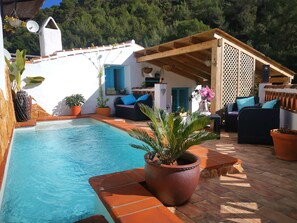 Una zona de piscina con terraza de madera, mobiliario exterior y plantas en macetas.