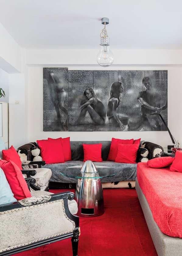 A living room with a sofa, red cushions, a vintage chair, a metallic coffee table, and a large abstract painting on the wall.