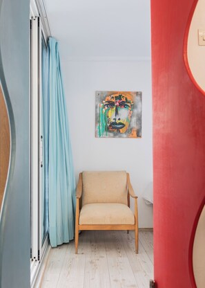 A room with a wooden chair, a blue curtain, and a painting on the wall.