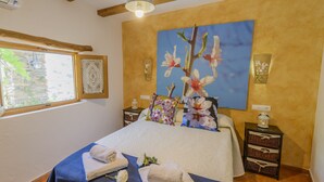 Een slaapkamer met een bed, een raam met uitzicht, een nachtkastje en een wandlamp.