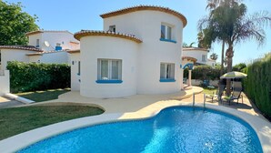 A pool area with a curved pool, a white building with blue trim, and a palm tree.
