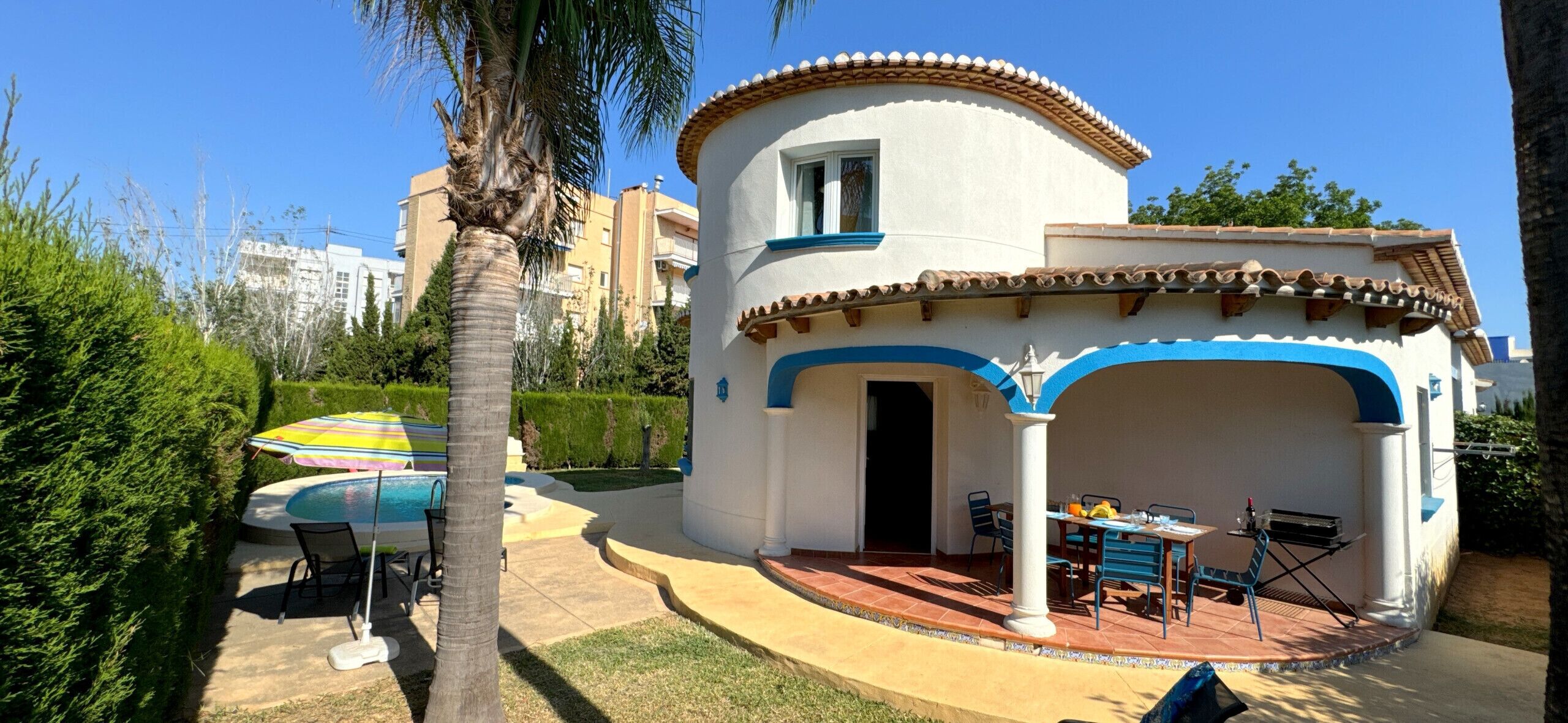 A white building with blue accents, a pool, and outdoor seating.