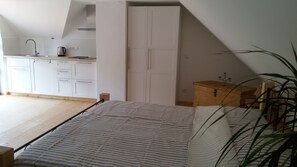 Ein Schlafzimmer mit einem Bett, einer Holzkommode und einer Küchenzeile mit Schränken und einem Wasserkocher.