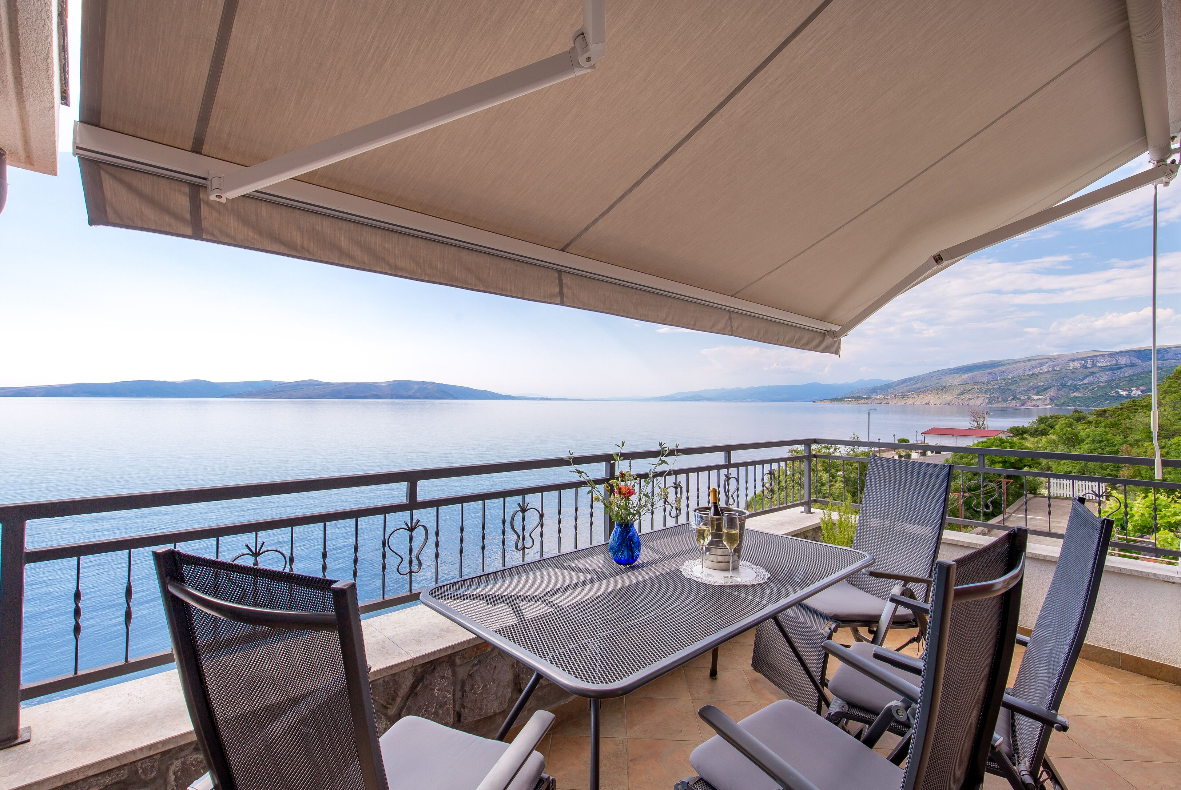 Una terrazza con tavolo, sedie e vista su uno specchio d'acqua e montagne in lontananza.