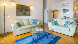 Un salon avec deux canapés blancs, une table basse en verre, un tapis bleu et un tableau accroché au mur.
