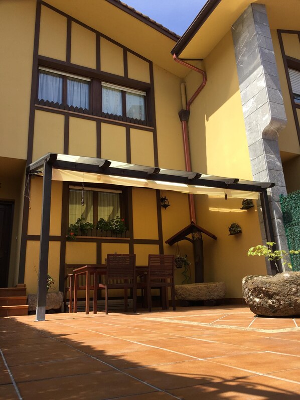 Un bâtiment à deux étages avec une façade jaune, un patio couvert avec une table et des chaises, et des plantes en pot.