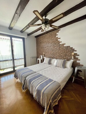 Une chambre dotée d’un grand lit, d’un ventilateur de plafond, d’un mur décoratif en briques et donnant sur l’extérieur grâce à une porte vitrée.