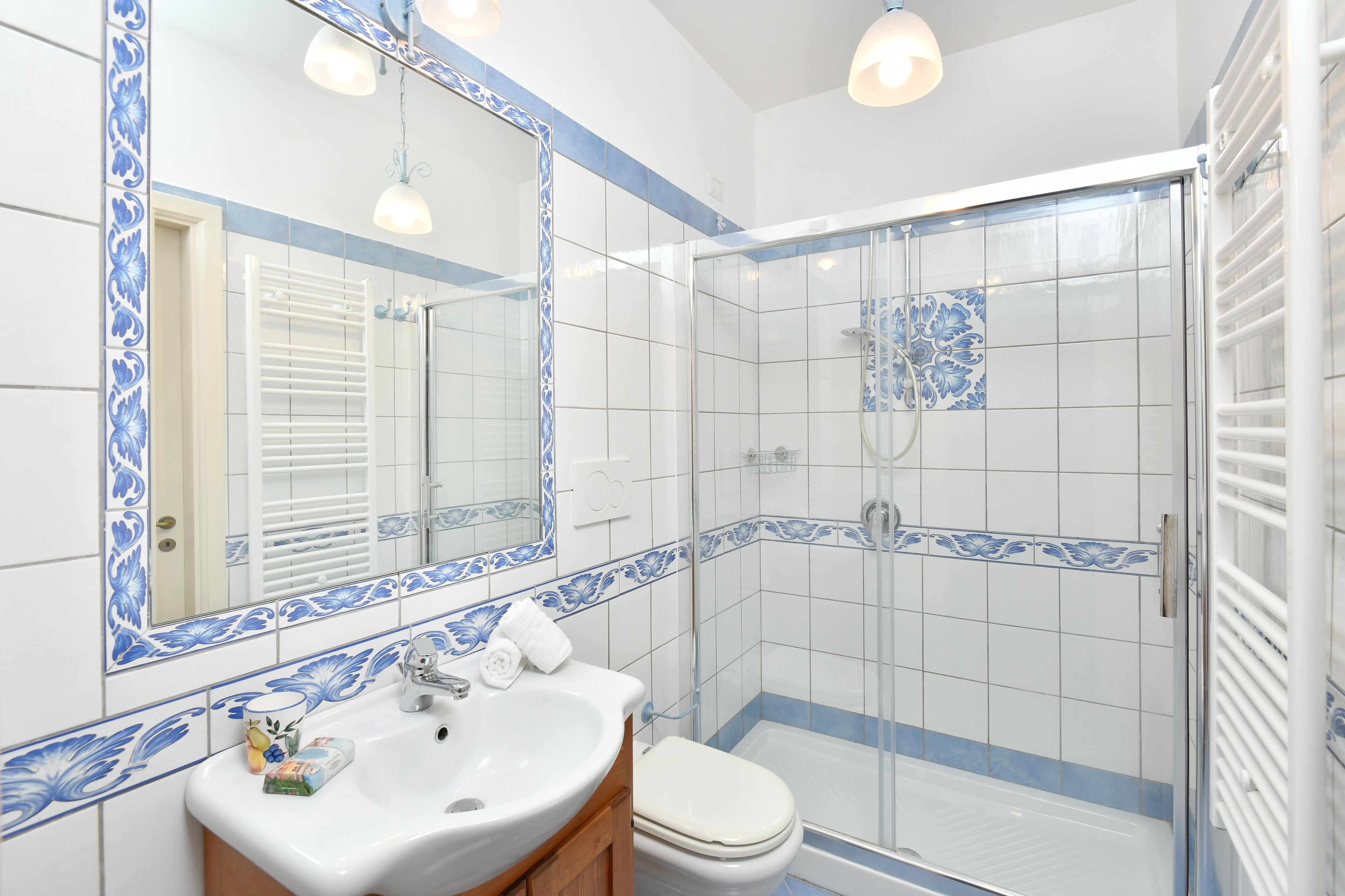 A bathroom with a white sink, a toilet, a shower with a glass door, and a mirror with a blue decorative border.