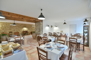 Uma sala de jantar com várias mesas postas para refeições, cadeiras de madeira e luminárias pendentes.